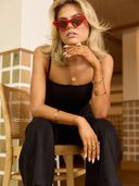Woman wearing red sunglasses and a black outfit sitting on a wooden chair.